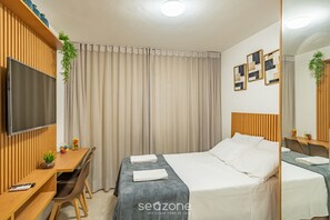 A hotel room with a bed, a desk, a TV, and a window with curtains.