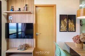A modern living room with a flat-screen TV, wooden shelves, a door, and wall art.