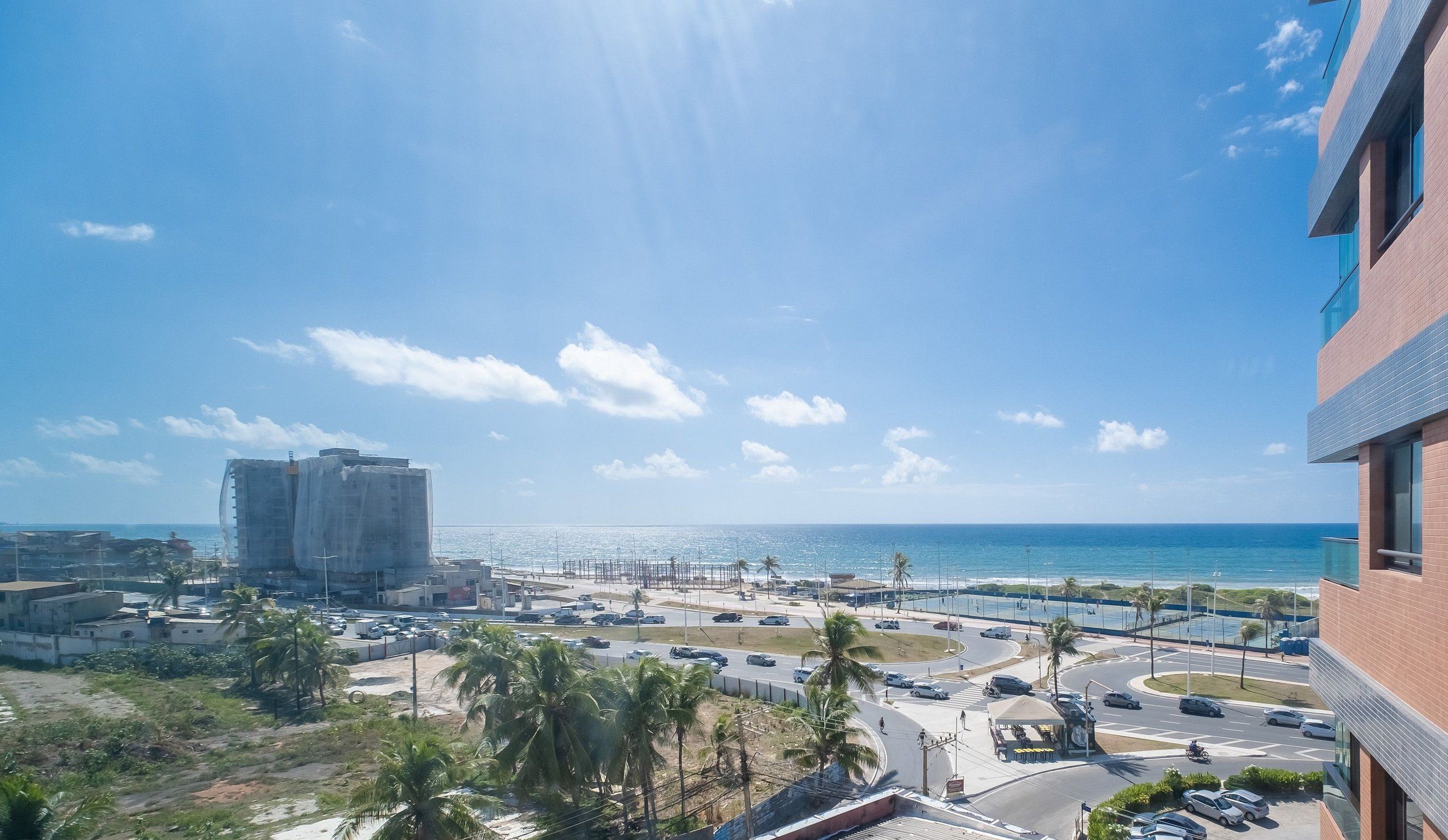 A coastal cityscape with a view of the ocean, a busy road with vehicles, and a large building in the background.