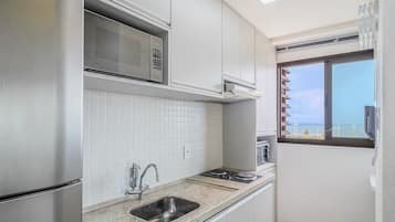 A kitchen with white cabinets, a microwave, a sink, and a window with a view of the sea.