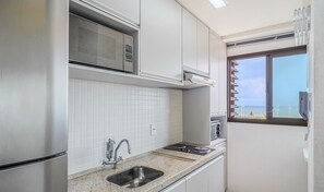 Una cocina con armarios blancos, microondas, fregadero y ventana con vista al mar.