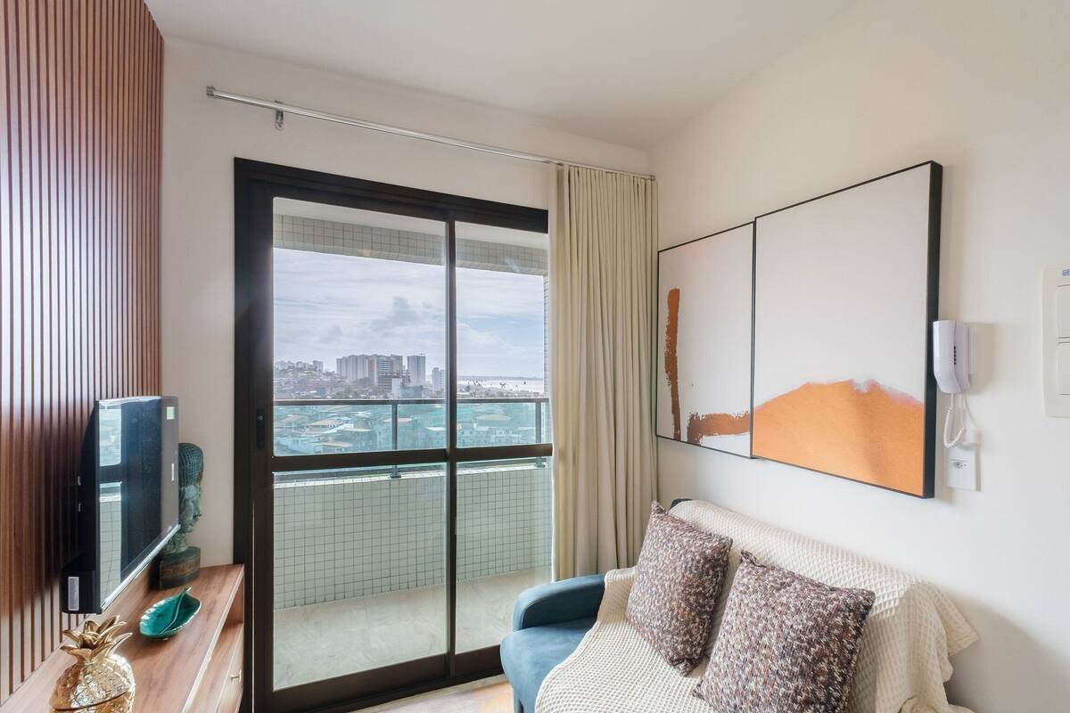 Et hotelværelse med en stor skydedør til en balkon, et fladskærms-tv, en dekorativ ananas og et indrammet abstrakt maleri.