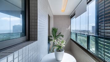 Um banheiro moderno com vista para a cidade através de grandes janelas, parede com azulejos brancos e uma planta em vaso sobre um pedestal branco.