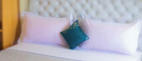 Un lit avec une tête de lit capitonnée, une literie blanche et un plaid turquoise.