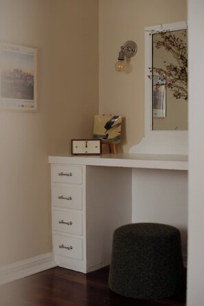 A corner of a room with a white dresser, a clock, a framed picture, and a mirror reflecting a floral arrangement. - Studio in the heart of Hollywood (Los Angeles)