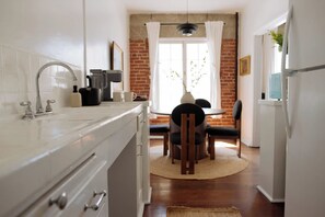 A kitchen with white cabinets, a sink, and a dining area with a table and chairs. - Studio in the heart of Hollywood (Los Angeles)