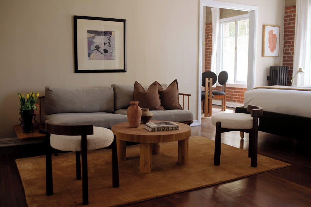 A living room with a sofa, two armchairs, a coffee table, and a bookshelf. There is a framed picture on the wall and a window with a view of the outside.