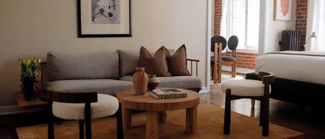 A living room with a sofa, two armchairs, a coffee table, and a bookshelf. There is a framed picture on the wall and a window with a view of the outside.