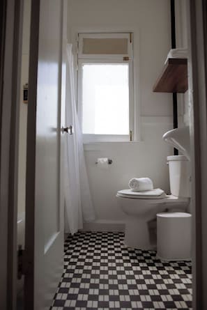 A narrow bathroom with a checkered floor, a toilet, a small window, and a towel on the seat.