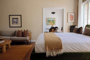 A bedroom with a large bed, a sofa, a small table, and artwork on the walls.
