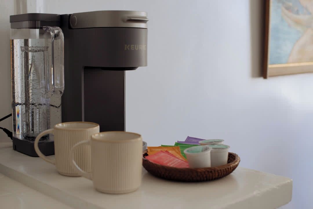 Una cafetera Keurig, dos tazas y una cesta con cápsulas de café sobre una encimera.