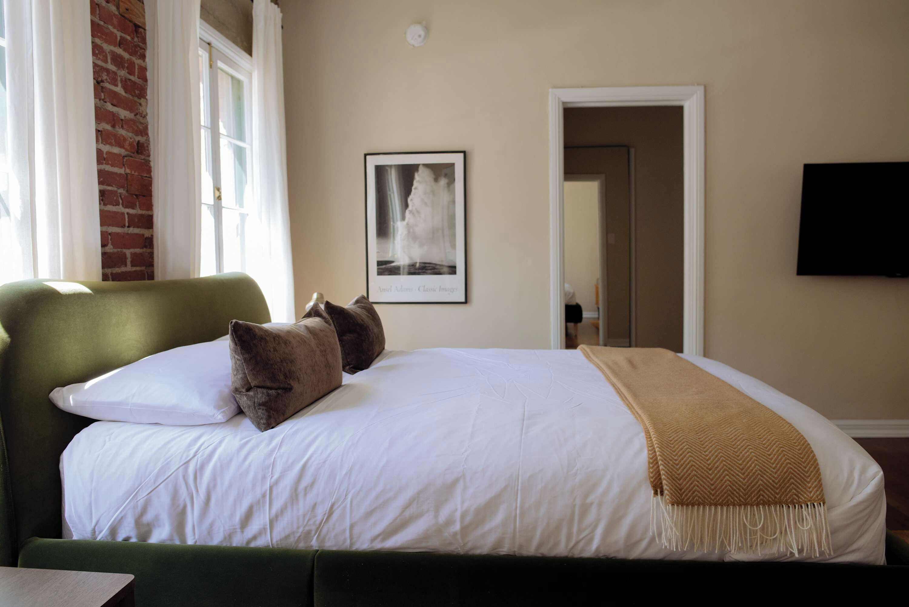 Een bed met witte lakens, een groen hoofdbord en een bruine plaid.