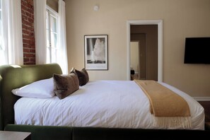 A bed with white linens, a green headboard, and a brown throw blanket.