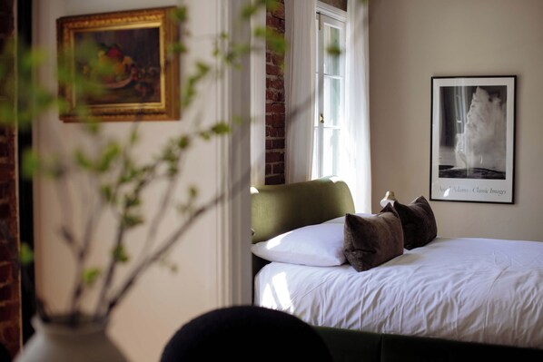 A bedroom with a green headboard, white bedding, and a framed picture on the wall.