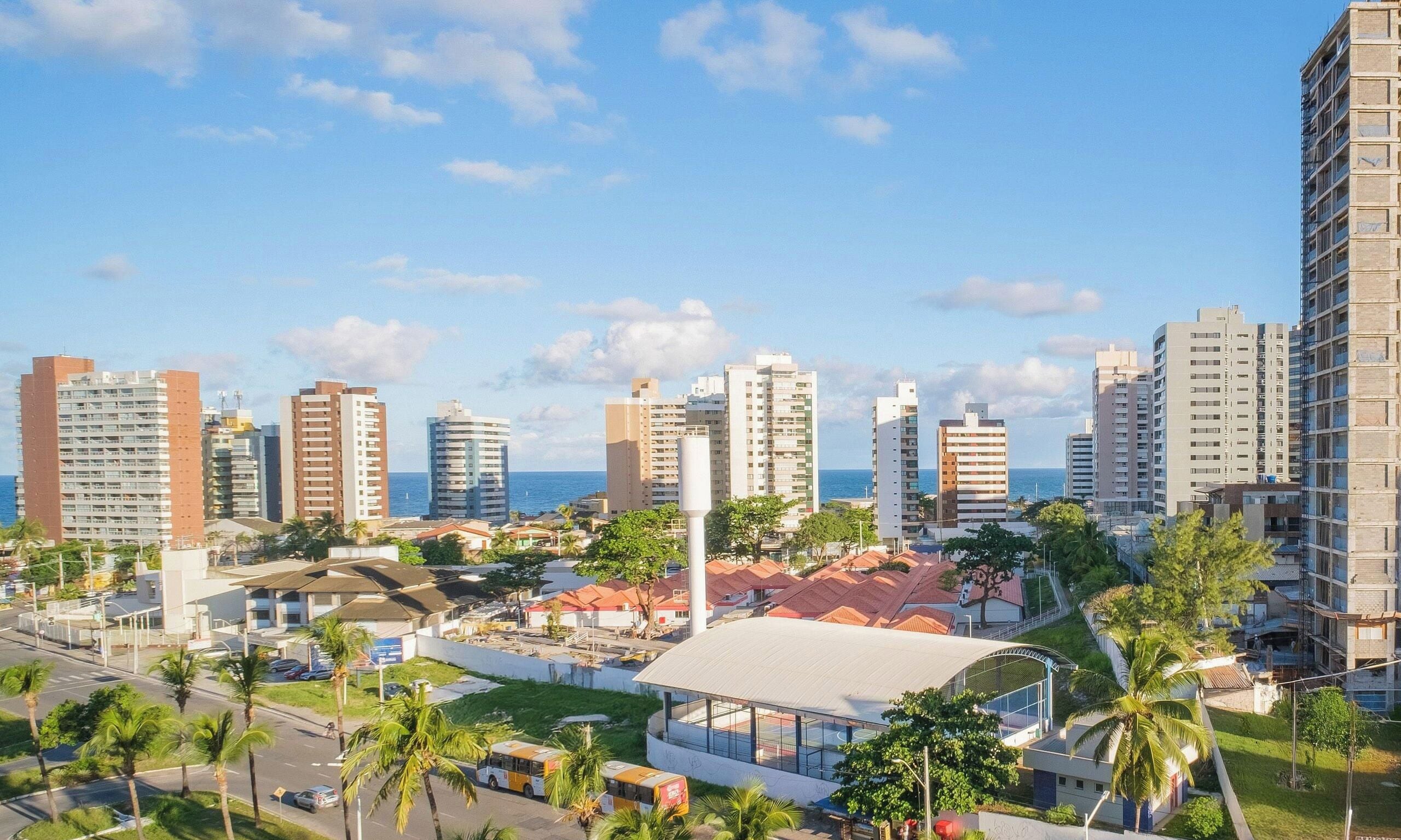 A coastal cityscape with high-rise buildings, a sports complex, and palm trees.