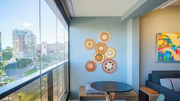 A balcony with a view of a cityscape, a round table with a cushion, and a wall with circular woven decorations.