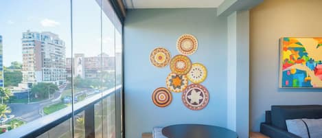 A balcony with a view of a cityscape, a round table with a cushion, and a wall with circular woven decorations.