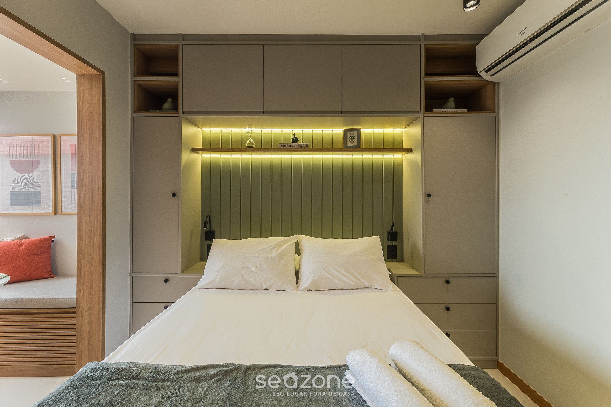 A bedroom with a bed, bedside tables, a built-in shelf, and an air conditioning unit.