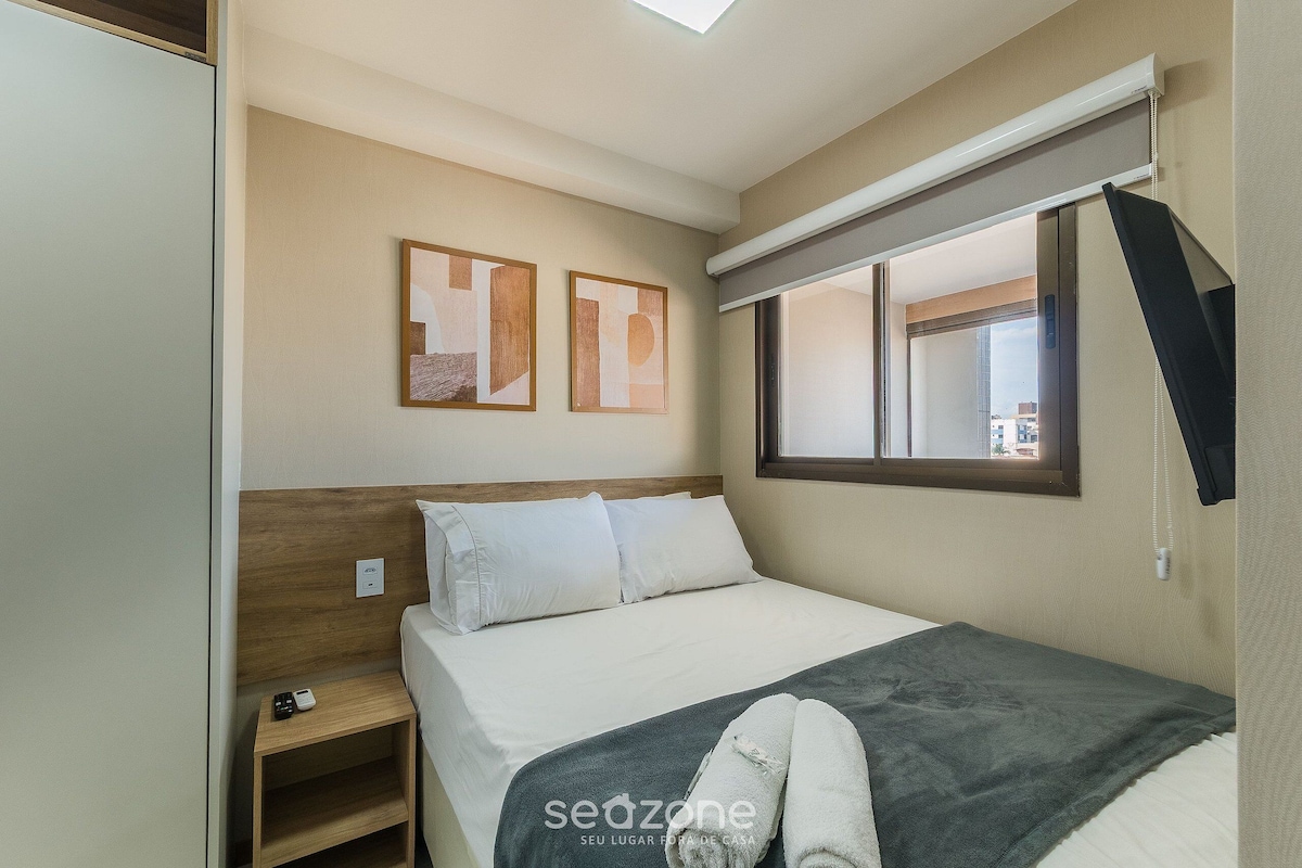 Une chambre d’hôtel avec un lit, une table de chevet, une fenêtre avec des stores et deux tableaux abstraits accrochés au mur.