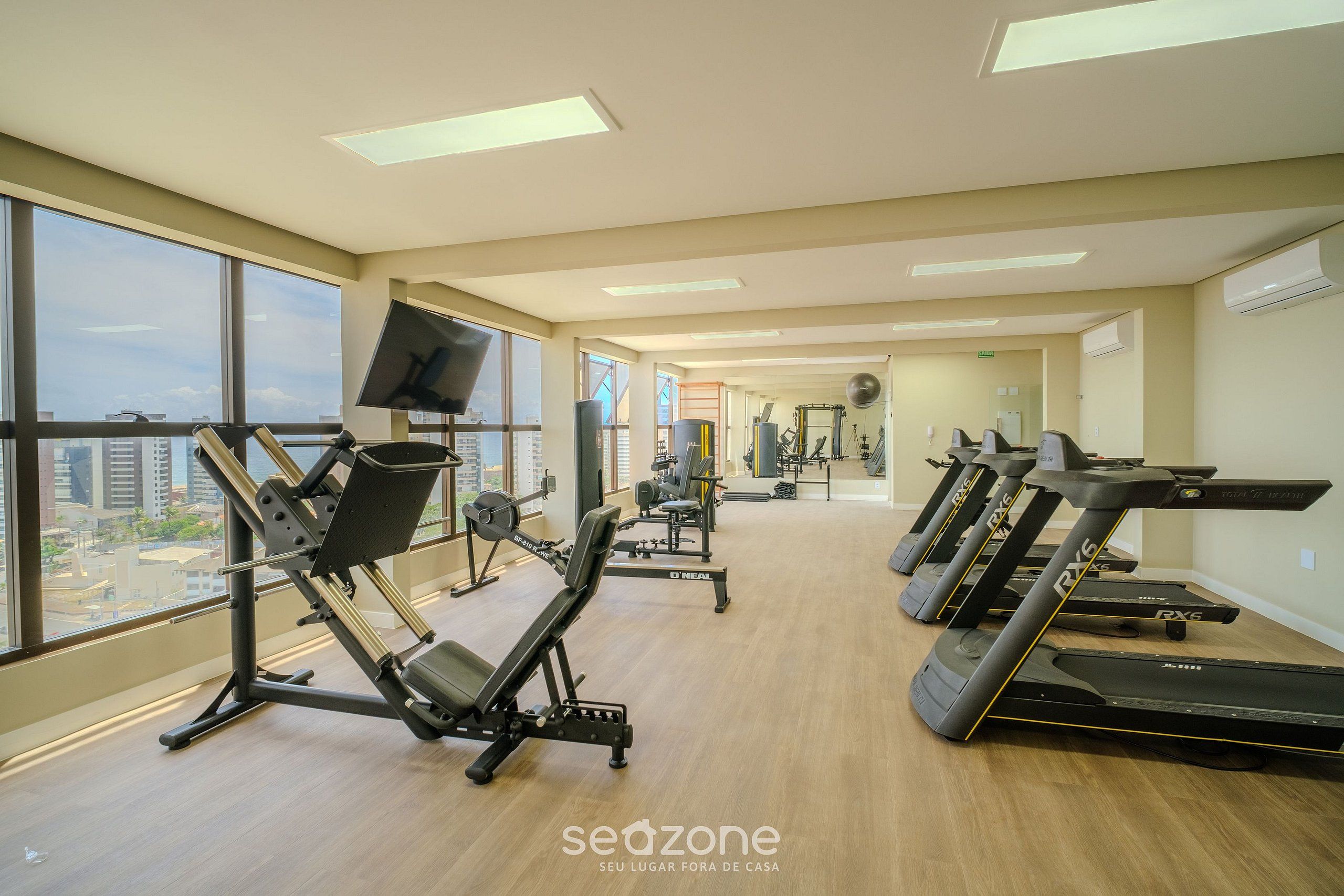 Ein Fitnessstudio mit Laufbändern, Kraftgeräten und einem Bildschirm.