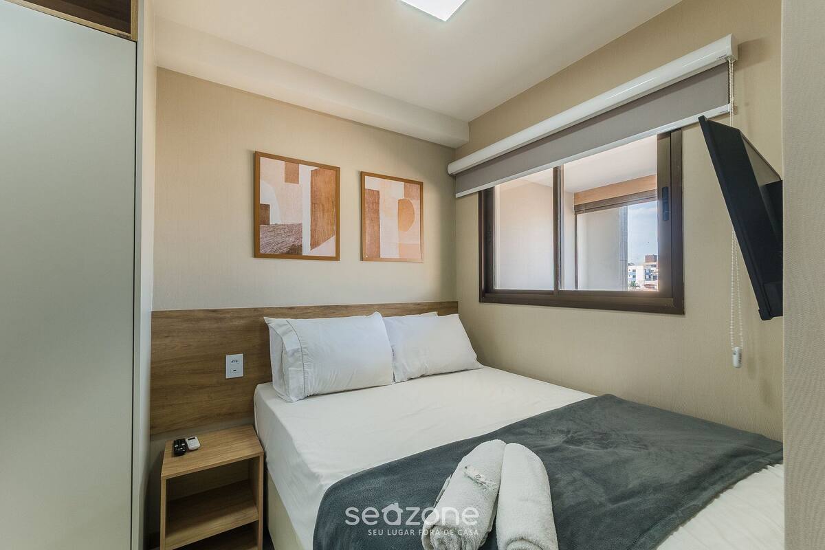 A hotel room with a bed, a bedside table, a window with blinds, and two abstract paintings on the wall.