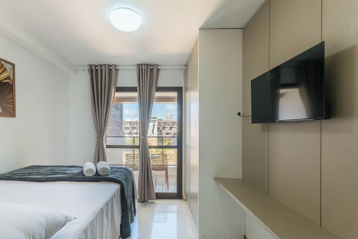 Une chambre d’hôtel avec un lit, un téléviseur à écran plat fixé au mur, un balcon avec des rideaux et une vue sur la ville.