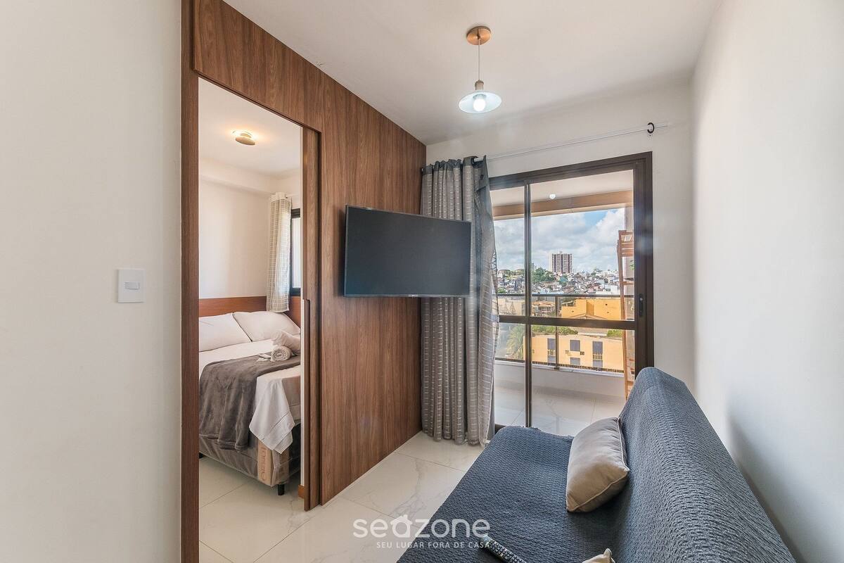 A modern room with a bed, a sofa, a TV, and a balcony with a city view.