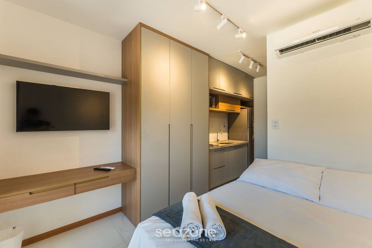 A modern bedroom with a bed, a TV, a wardrobe, and a small kitchenette.