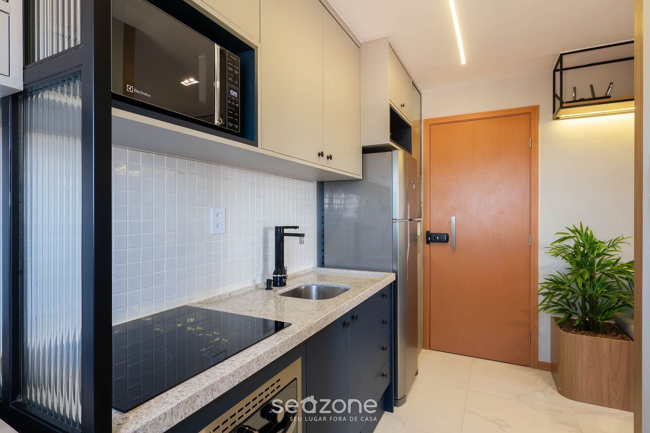 A modern kitchen with a built-in microwave, stainless steel sink, and a wooden door.