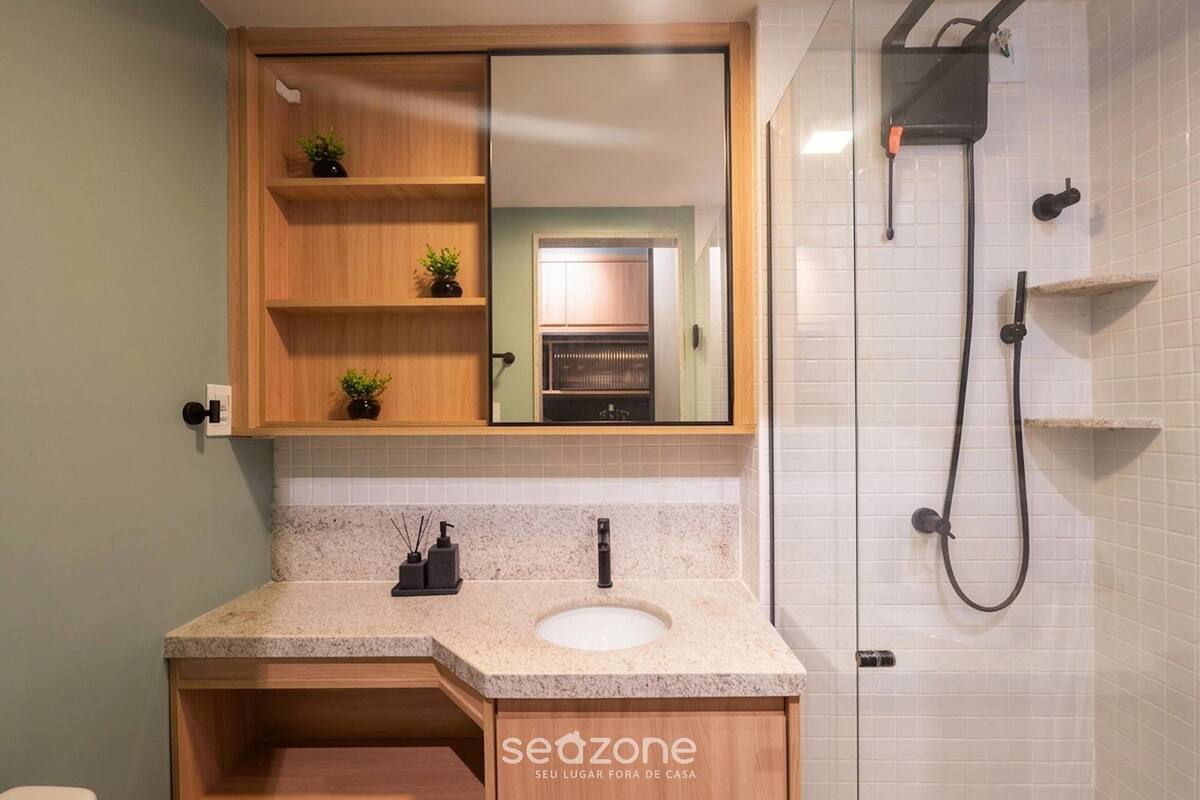 A bathroom with a wooden vanity, a sink, a mirror, a shower, and a tiled wall.