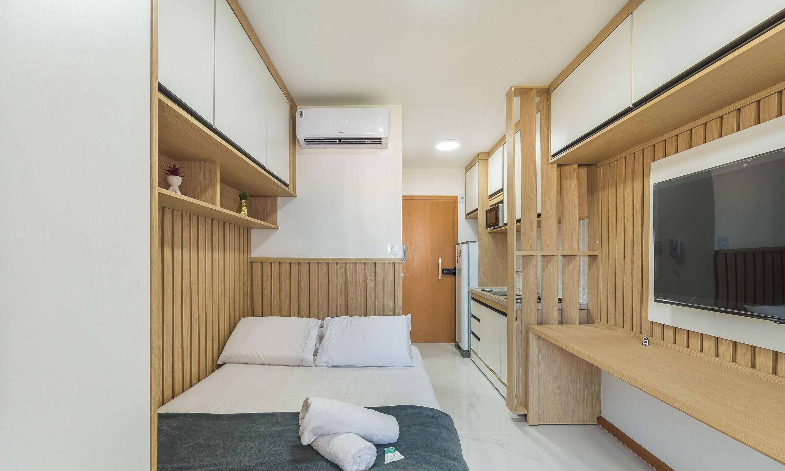 Een kleine hotelkamer met een bed, een kitchenette, een ingebouwde televisie en een raam.