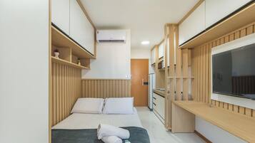 Een kleine hotelkamer met een bed, een kitchenette, een ingebouwde televisie en een raam.
