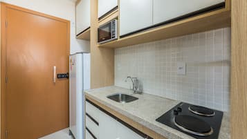 Cocina compacta con microondas, lavabo y estufa, armarios de madera y salpicadero de azulejos.