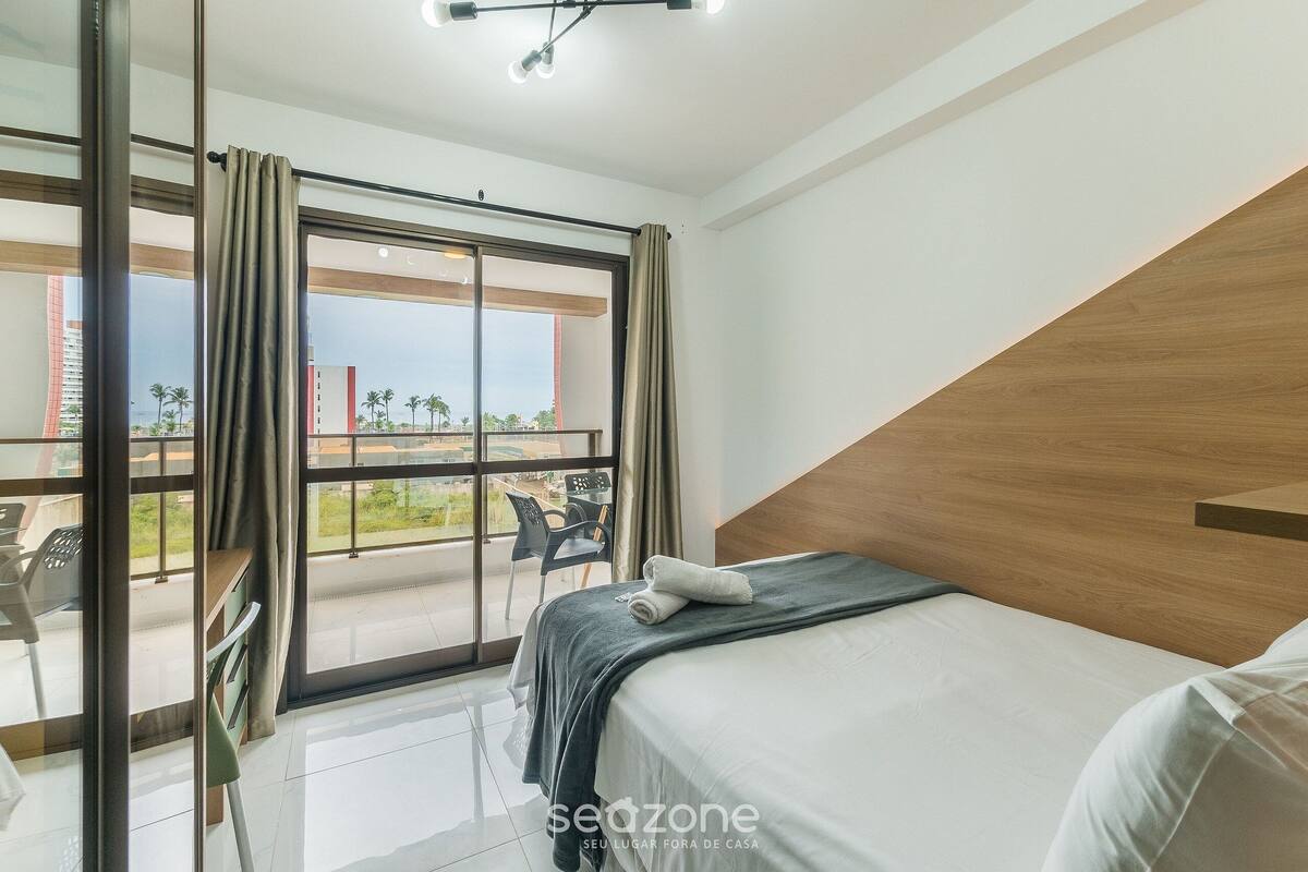 A hotel room with a bed, a view of the outside, and a balcony with chairs.