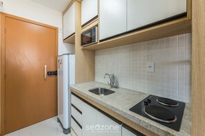A compact kitchen with a microwave, sink, and stove, wooden cabinets, and a tiled backsplash. - SMT - Building 750m From the Beach in Salvador (Salvador)