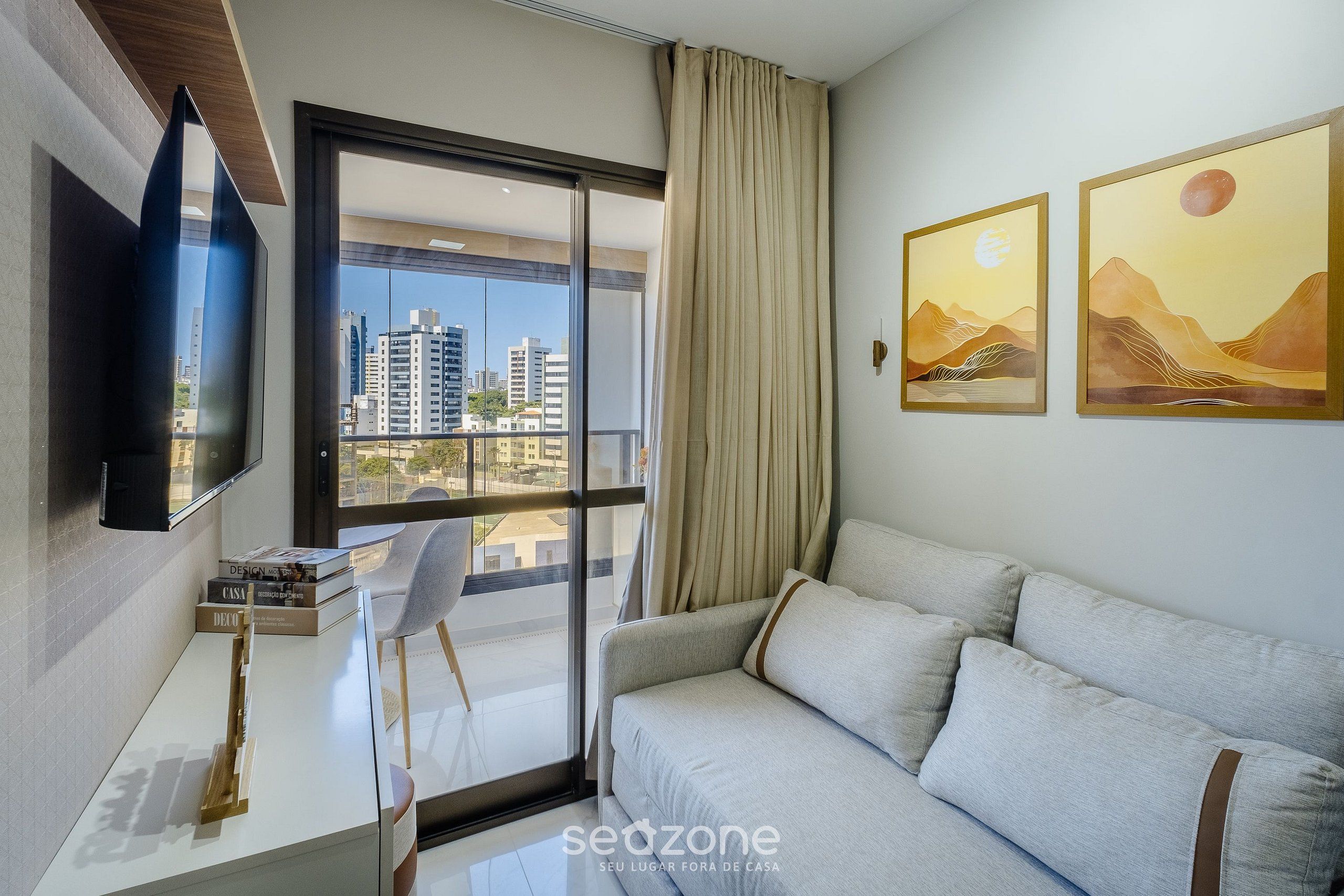 A modern living room with a sofa, a flat-screen TV, a desk with books, and a large window with a city view.