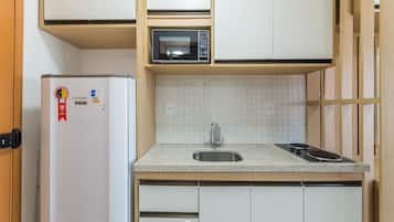 Una cocina compacta con microondas integrado, un lavamanos de acero inoxidable y un refrigerador blanco.