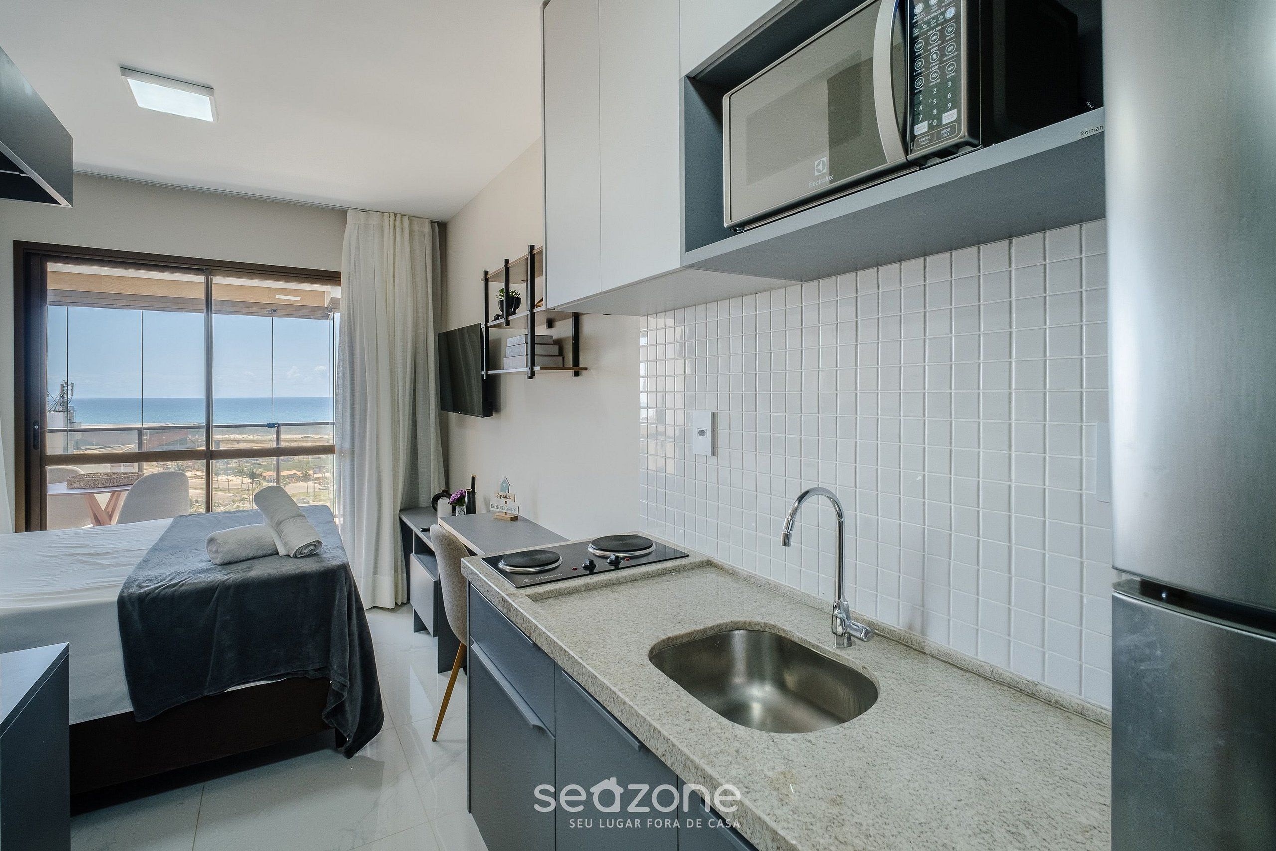 Een moderne hotelkamer met een bed, kitchenette en uitzicht op zee.