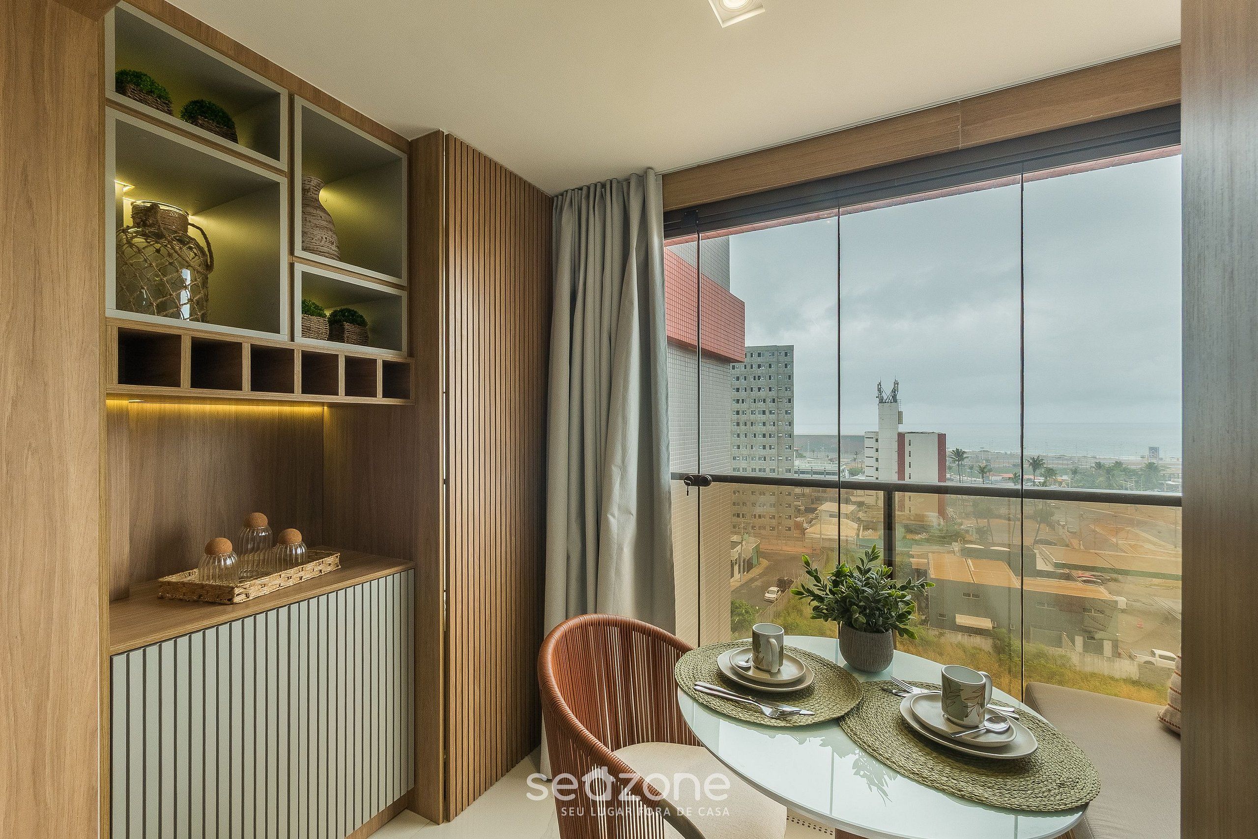 Een moderne kamer met een eettafel, stoelen, een potplant en uitzicht op de stad door grote ramen.