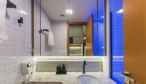 Une salle de bain avec un lavabo blanc, un miroir, un porte-serviettes et un espace douche aux carreaux bleus.