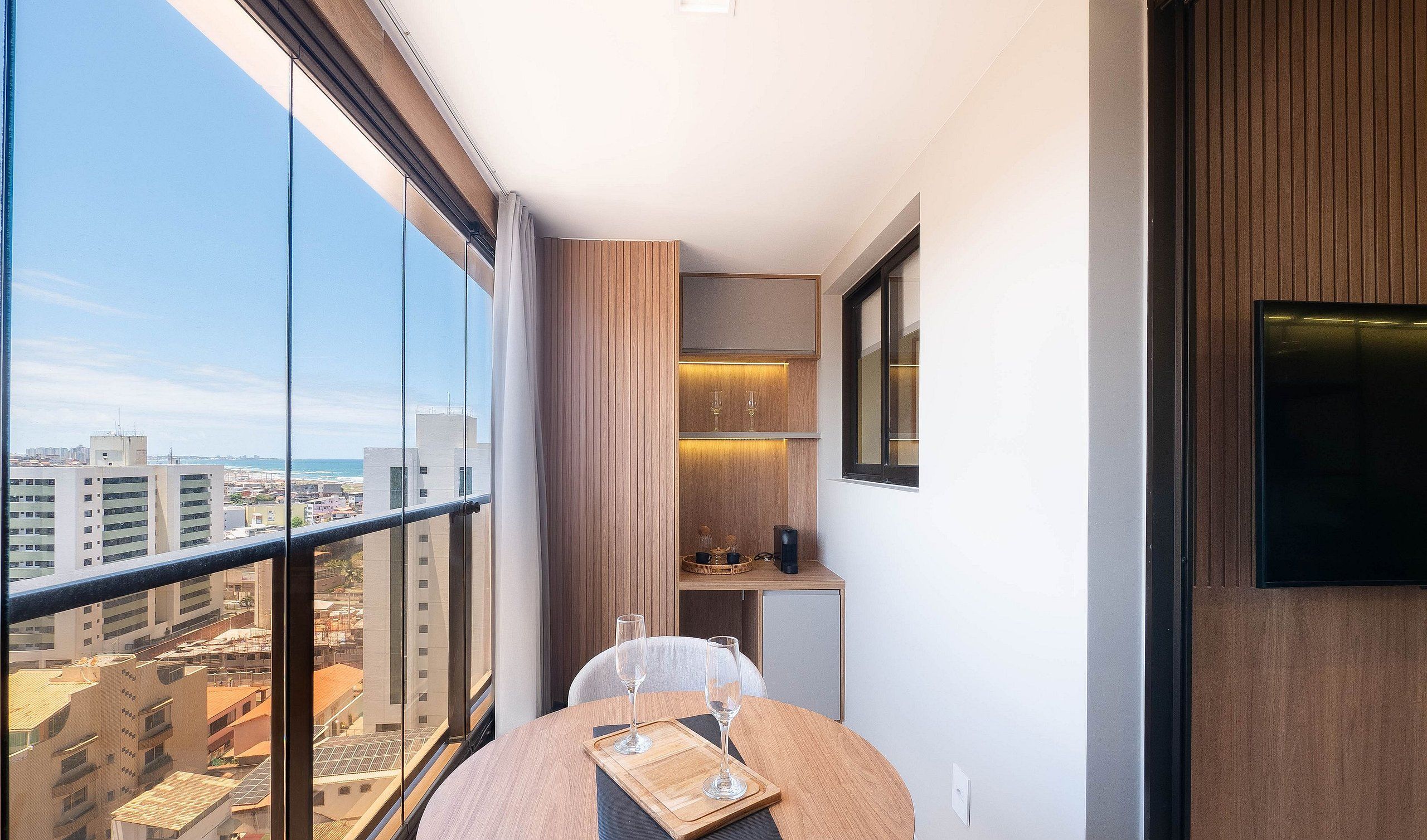 A balcony with a city view, a small table with glasses, and a TV on the wall.