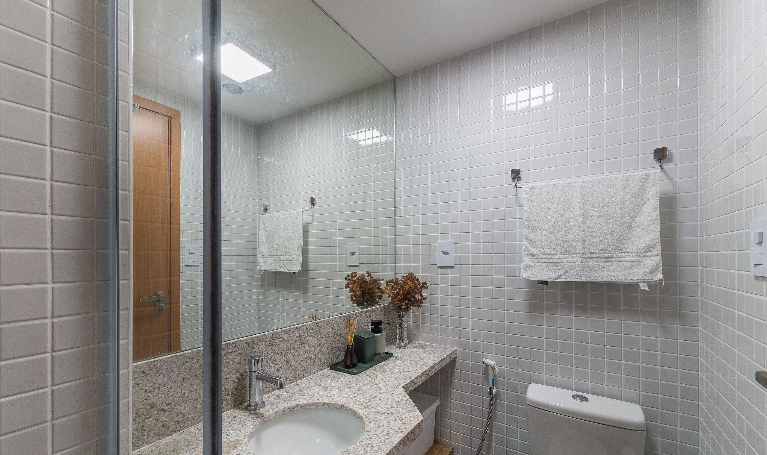 Een badkamer met witte betegelde wanden, een wastafel, een toilet en een spiegel.