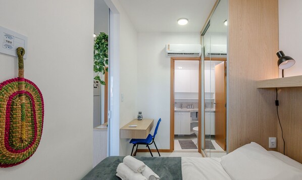 A compact hotel room with a bed, a desk, a chair, a mirror, and a wall-mounted air conditioner. - SMT - Building 750m From the Beach in Salvador (Salvador)