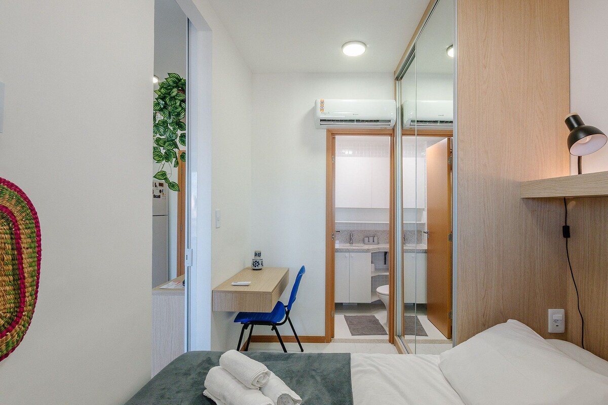 Ein kleines Hotelzimmer mit Bett, Schreibtisch, Stuhl, Spiegel und einer Wandklimaanlage.