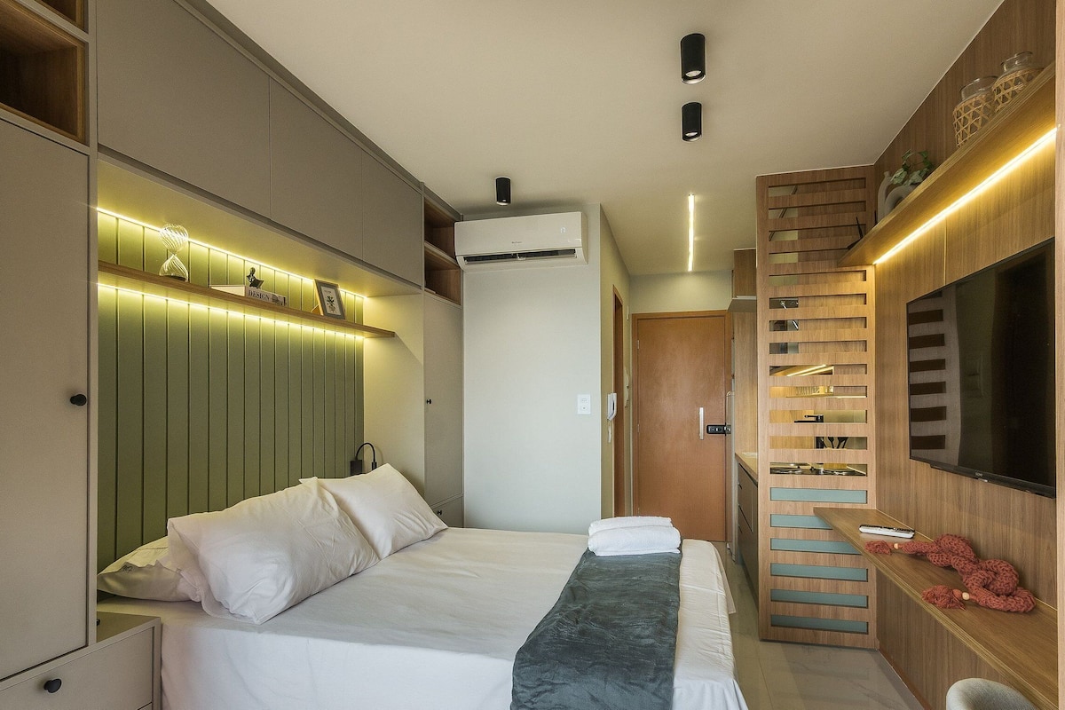 A modern hotel room with a bed, a TV, a built-in wardrobe, and a wall-mounted shelf with decorative items.