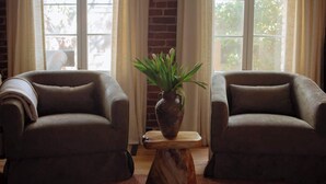 Two armchairs facing each other with a wooden coffee table between them, a potted plant on the table, and a brick wall in the background.