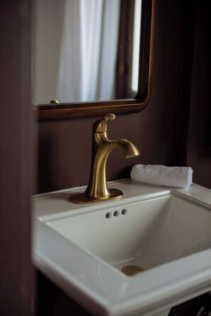 Een badkamer met een witte wastafel, een gouden kraan en een spiegel erboven.