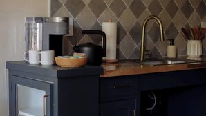 A kitchen with a dark blue cabinet, a coffee maker, a kettle, and a sink with a gold faucet.