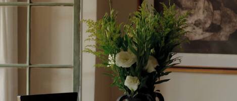 A round table with a vase of flowers, two chairs, a pendant light, and a framed picture on the wall.