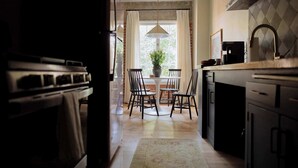 A kitchen with a central island, a dining table with chairs, a hanging light fixture, and a window with curtains.